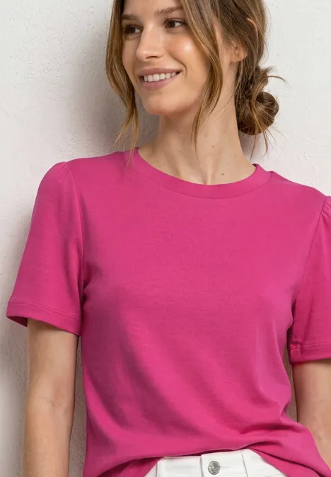 T-Shirt mit gerafftem Ärmel magenta dream Frau in pinkem T-Shirt und weißer Hose vor hellem Hintergrund, lächelnd.