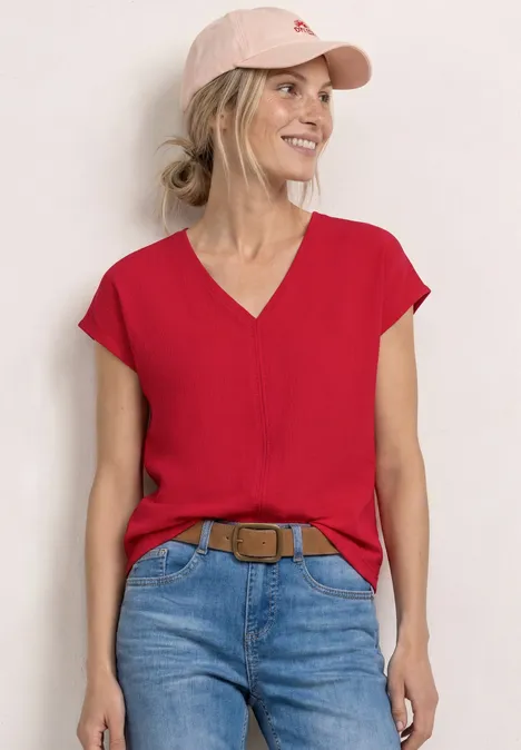 Vrouw in rood V-shirt, spijkerbroek en roze pet voor witte muur