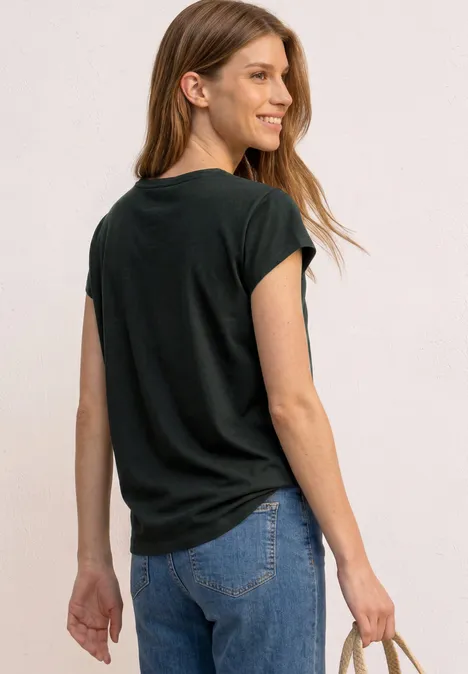 Vrouw gezien van achteren, met een zwart T-shirt, blauwe jeans en een gevlochten tas in de hand.