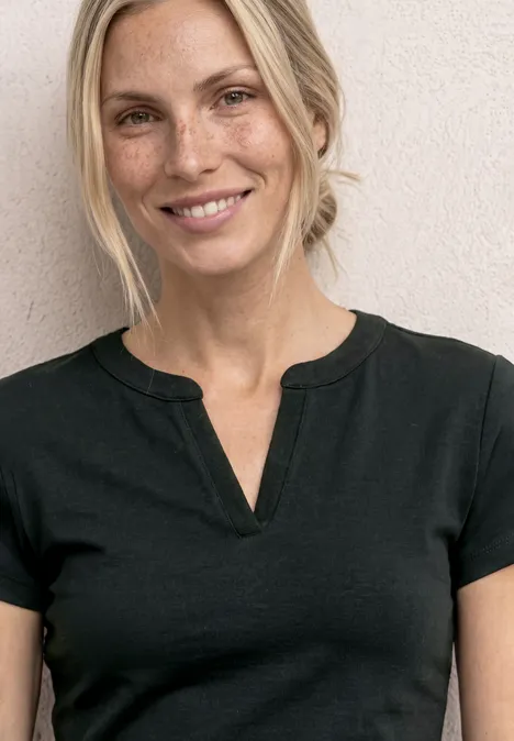 Frau trägt schlichtes schwarzes T-Shirt, Oberkörper bis Hals sichtbar, Gesicht unscharf.