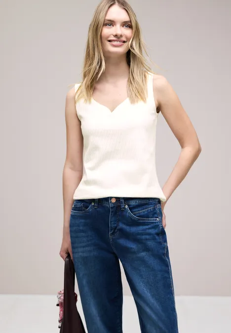 Frau in weißem Top und blauen Jeans hält eine Tasche, Gesicht unscharf.