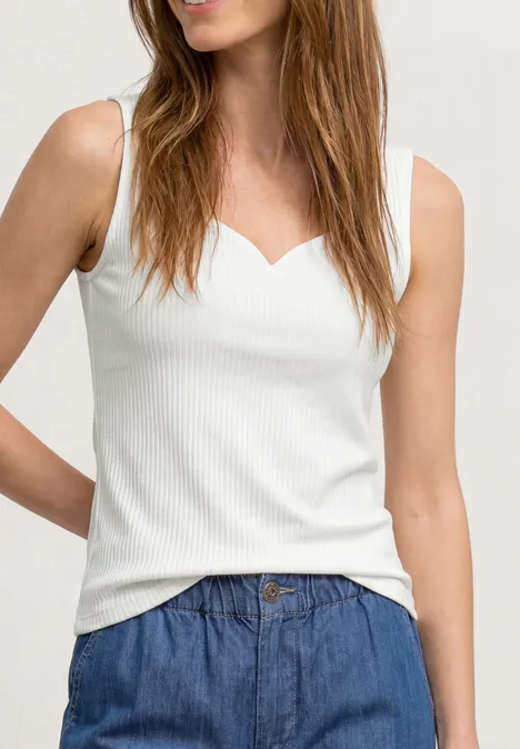 Femme en débardeur blanc côtelé à encolure cœur et pantalon en jean bleu.