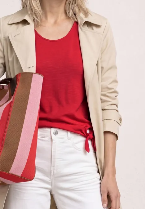 Kurzarm Shirt mit Knotendetail salsa red Frau im rot geknoteten Top, weißer Hose, beigem Mantel und gestreifter Tasche