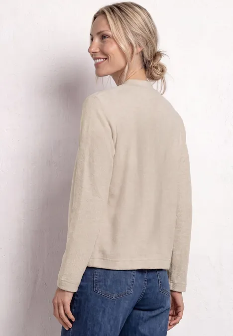 Rückenansicht einer Person mit beigem Pullover und blauer Jeans vor hellem Hintergrund.