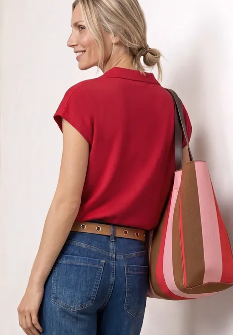 Eine von hinten gesehene Frau in roter Bluse, Jeans und Gürtel trägt eine gestreifte Schultertasche.