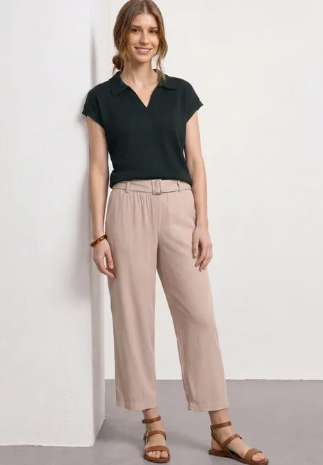 Frau in schwarzem Poloshirt und beiger Hose mit Ledergürtel und Sandalen