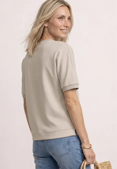 Vrouw van achteren in beige T-shirt met korte mouwen en blauwe jeans, met een strooien tas.