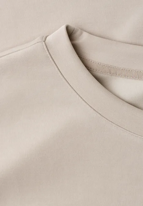 Close-up van een beige T-shirt met ronde hals en nette naden