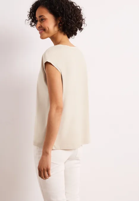 Seitliche Aufnahme einer Person in beigem Oberteil und weißer Hose.