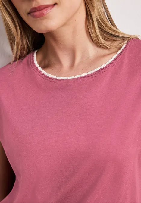 Een vrouw draagt een roze shirt met ronde hals afgewerkt met fijne kantrand.