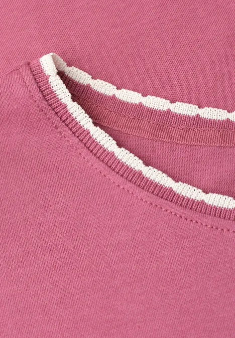 Close-up van een roze T-shirt met een wit, gegolfd biesje bij de halsuitsnijding.