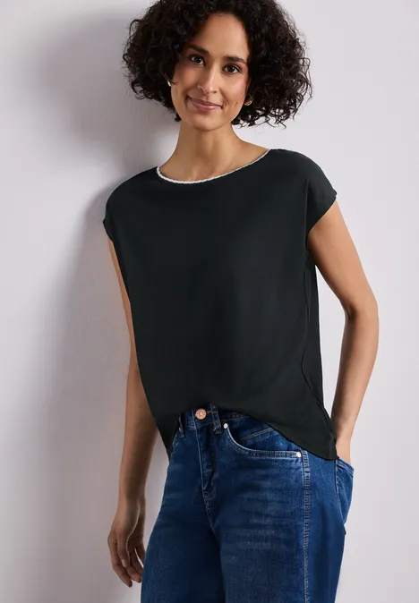 Vrouw draagt zwart t-shirt en blauwe jeans voor een witte achtergrond.
