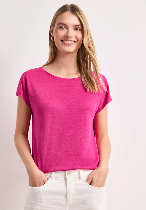 Vrouw met handen in de zakken, draagt roze T-shirt en witte broek voor lichte achtergrond.