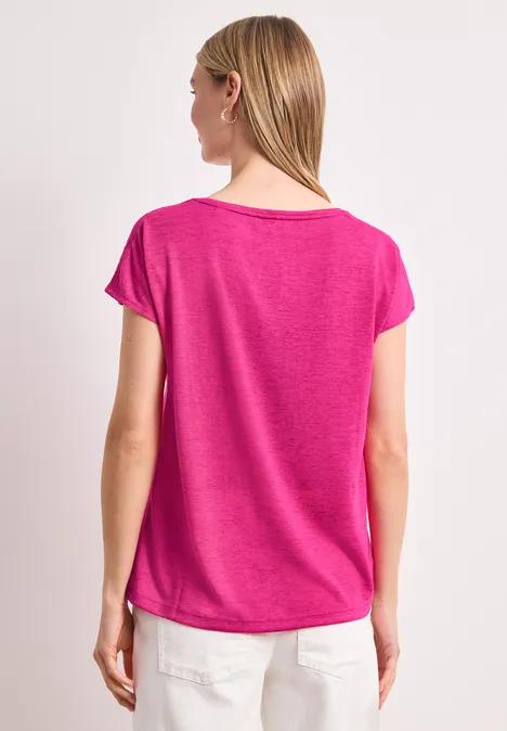 Vrouw van achteren in een roze t-shirt en witte broek tegen een witte achtergrond.