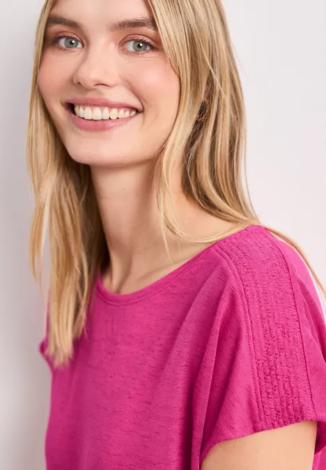 Persoon met blond haar draagt roze shirt voor lichte achtergrond.