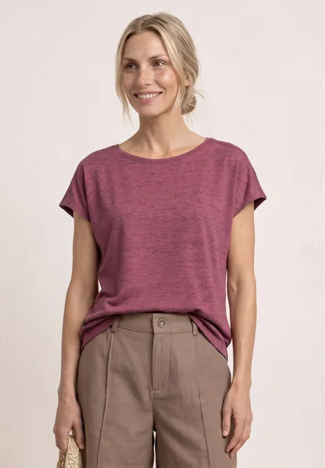 Een persoon met een wazig gezicht draagt een loszittend roze T-shirt en een beige broek.