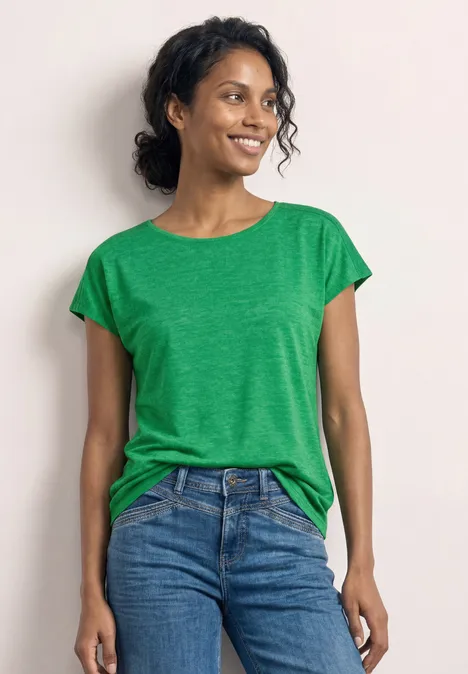 Vrouw in groen T-shirt en blauwe jeans voor een witte achtergrond.