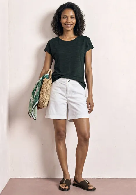 Vrouw in zwart shirt, witte short en sandalen met strooitas en gekleurde sjaal.