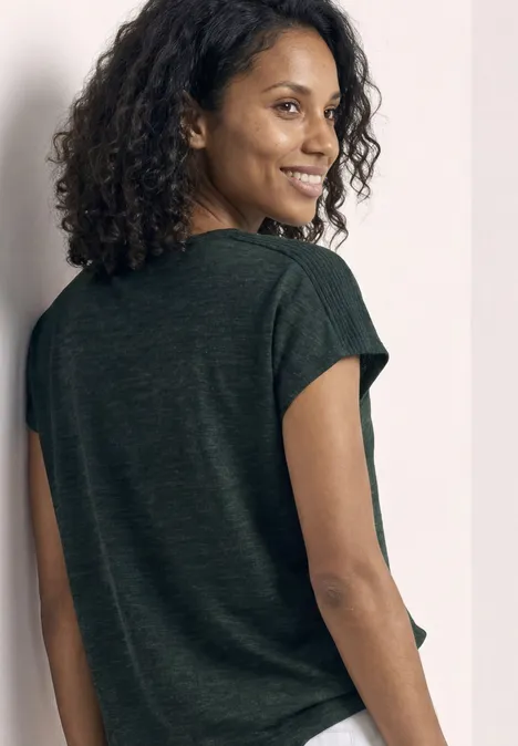 Persoon van achteren met krullend haar in een donkergroen T-shirt voor een lichte achtergrond.