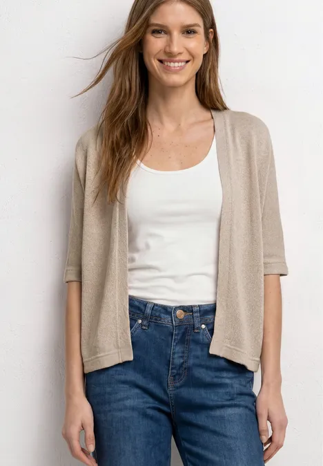 Vrouw met een witte tanktop, beige kortarmvest en blauwe high-waist jeans.