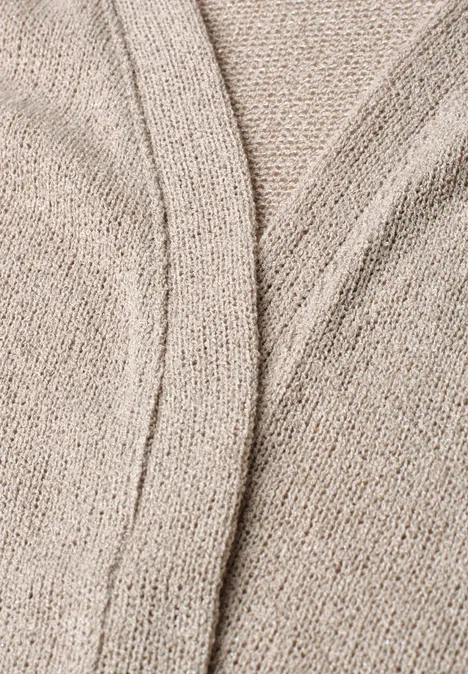 Close-up van een beige breiwerkstof met een subtiele sierlijke naad.