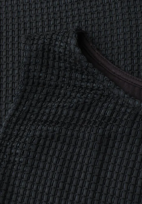 Close-up van donkergrijs gestructureerd gebreid textiel met ronde hals.