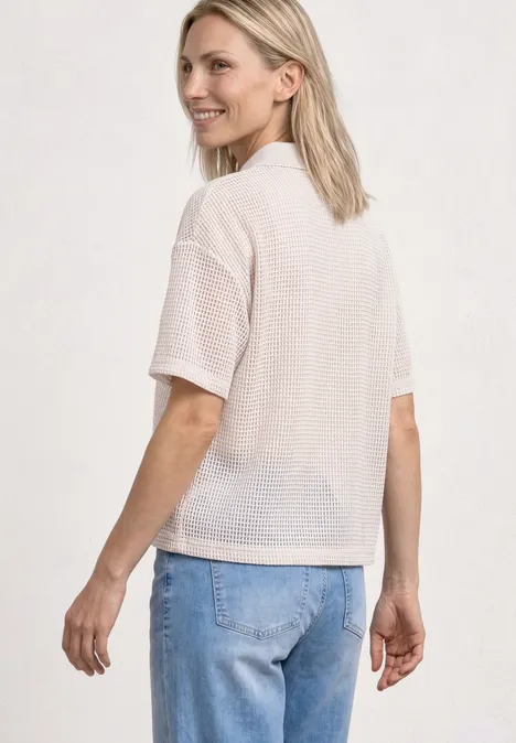 Frau von hinten in weißem Netzshirt und blauen Jeans.