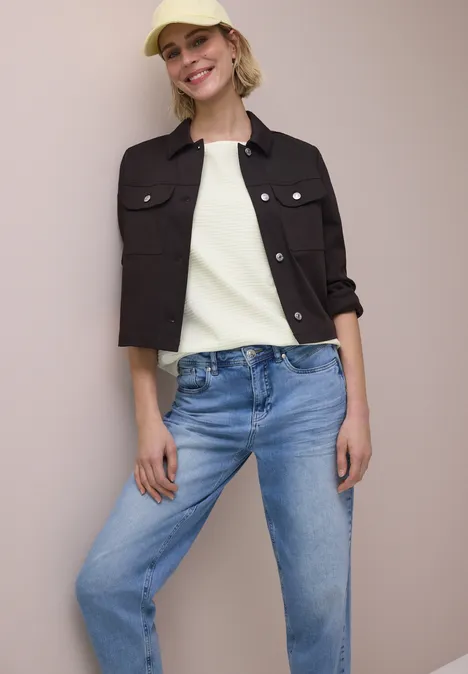 Frau trägt schwarze kurze Jacke, weißes Top und blaue Jeans.