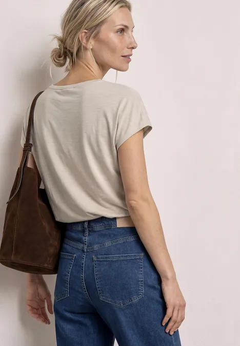 Vrouw van achter gezien met beige T-shirt en spijkerbroek, bruine schoudertas, haar in een knot.