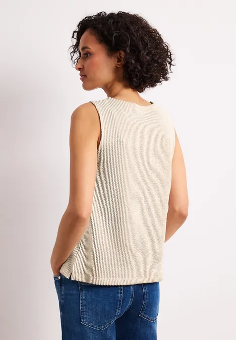 Person von hinten in beigem ärmellosem Top und blauen Jeans vor weißem Hintergrund.