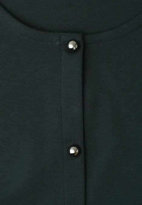 Nahaufnahme eines dunkelgrünen Oberteils mit zwei glänzenden Perlenknöpfen