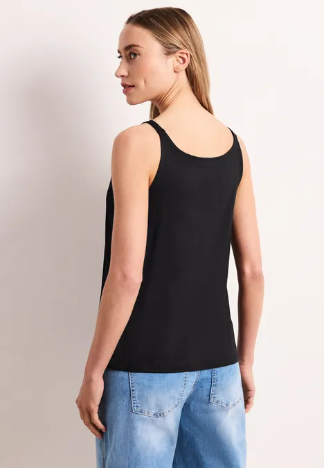 Rückenansicht einer Person in schwarzem Top und Jeans vor hellem Hintergrund.