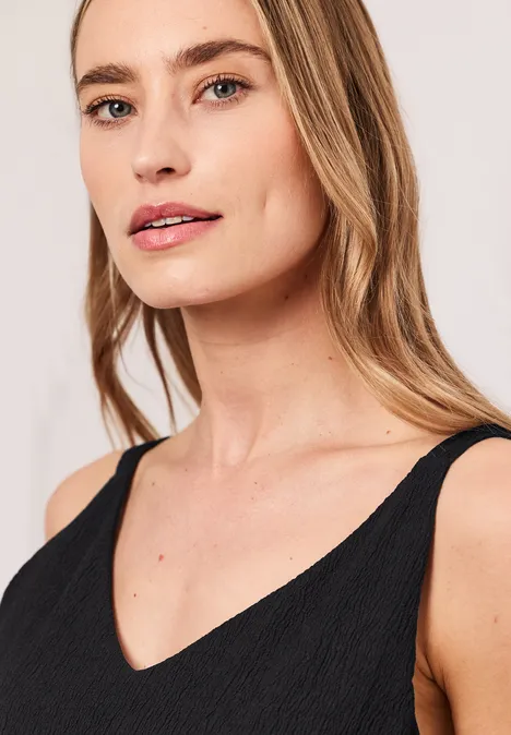 Porträt einer Frau mit blondem Haar in schwarzem ärmellosem V-Ausschnitt-Oberteil.