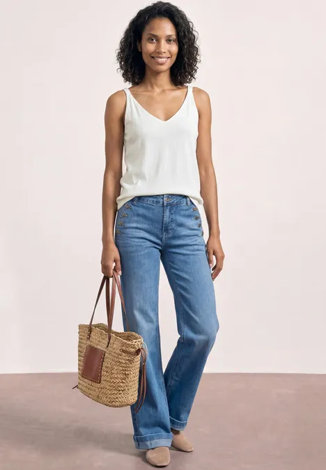 Eine Frau trägt ein weißes Top, weite blaue Jeans und hält eine geflochtene Korbtasche.