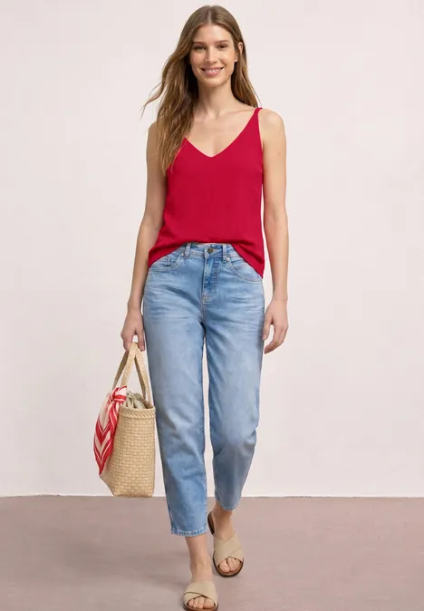 Frau in rotem Top und blauen Jeans mit Strohtasche und Sandalen.
