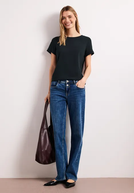 Persoon in zwart T-shirt, blauwe jeans en zwarte ballerina's, met een bruine tas.
