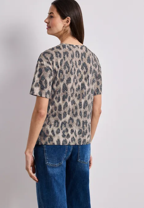 Frau von hinten in kurzärmeligem Leoparden-T-Shirt und blauen Jeans.