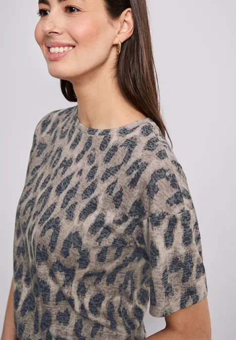 Frau in grauem Pullover mit dunklem Leopardenmuster vor hellem Hintergrund.