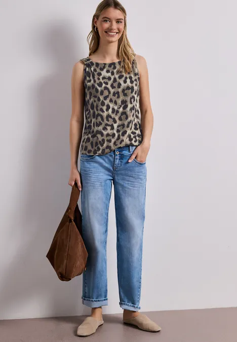 Frau trägt ärmelloses Leoparden-Top, blaue Jeans und braune Tasche.