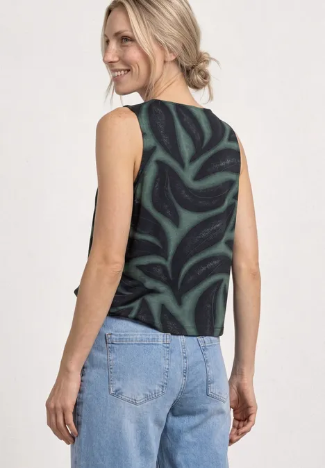 Frau von hinten in schwarzem, gemustertem Top und blauen Jeans vor hellem Hintergrund.