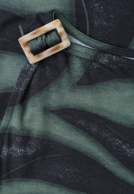 Nahaufnahme eines olivgrünen Stoffes mit dunklem Camouflage-Muster und einem eckigen hellen Schnallenverschluss.