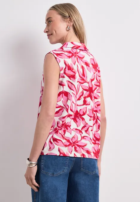 Femme de dos portant un haut sans manches à motif floral rose et blanc avec un jean.