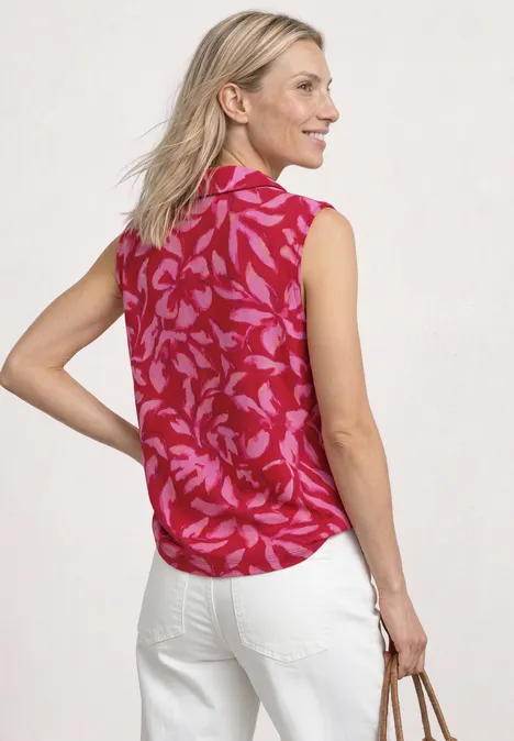 Frau von hinten in roter, ärmelloser Bluse mit Blumenmuster und weißer Hose