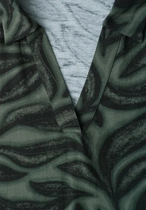 Top mit Kragen und Strukturmix deep bound green Nahaufnahme einer grünen Jacke mit abstraktem Wirbelmuster über einem grauen Shirt.