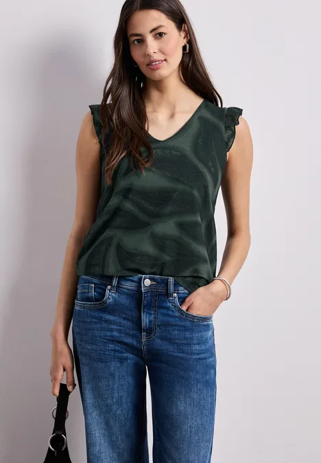 Frau mit grüner ärmelloser Bluse, blauen Jeans und kleiner schwarzer Handtasche