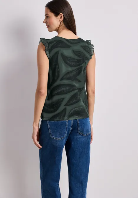 Frau von hinten mit grünem gemustertem Top und blauer Jeanshose.