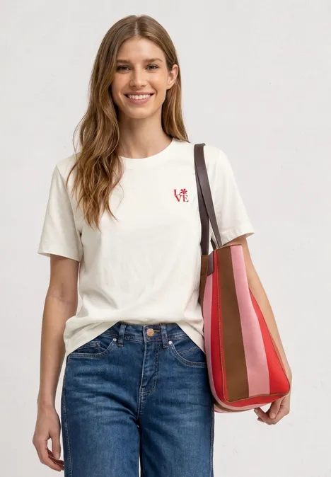 Junge Frau trägt weißes T-Shirt, Jeans und eine rot gestreifte Schultertasche.