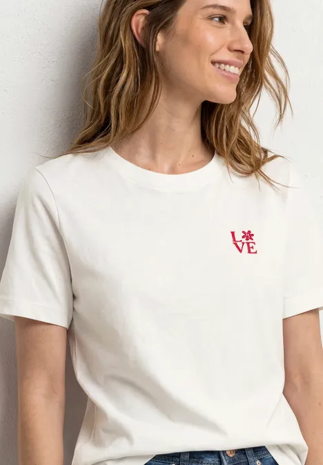 Frau trägt ein schlichtes weißes T-Shirt mit kleinem roten Schriftzug 'LOVE' auf der Brust.