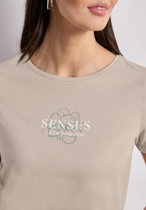 Nahaufnahme einer Frau in beigem T-Shirt mit floralem Logo und Schriftzug 'SENSES - take back your style'