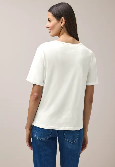 Persoon van achteren in wit T-shirt en blauwe spijkerbroek tegen neutrale achtergrond.